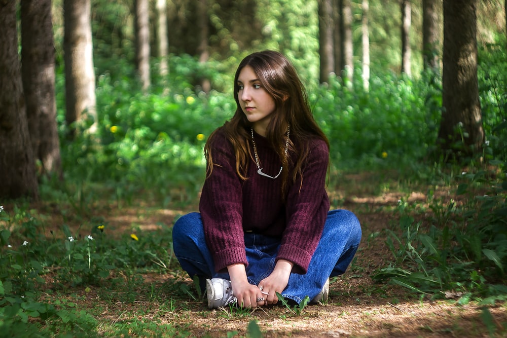 woman in brown sweater and blue denim jeans sitting on green grass during daytime