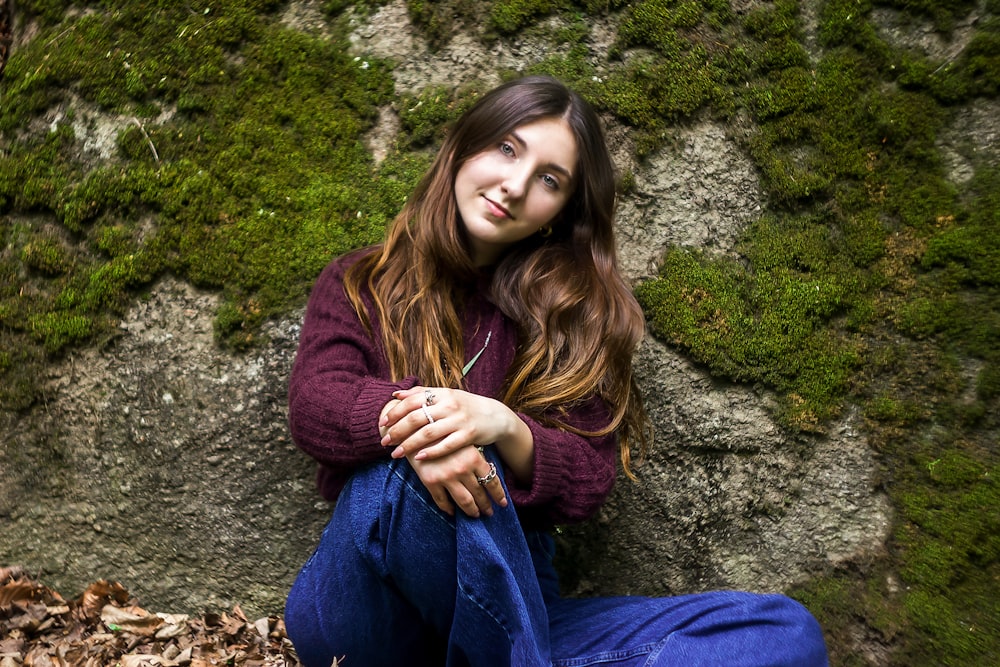 woman in purple sweater and blue denim jeans sitting on gray rock