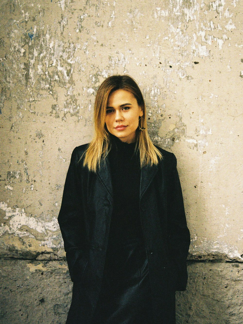 woman in black blazer standing beside white wall
