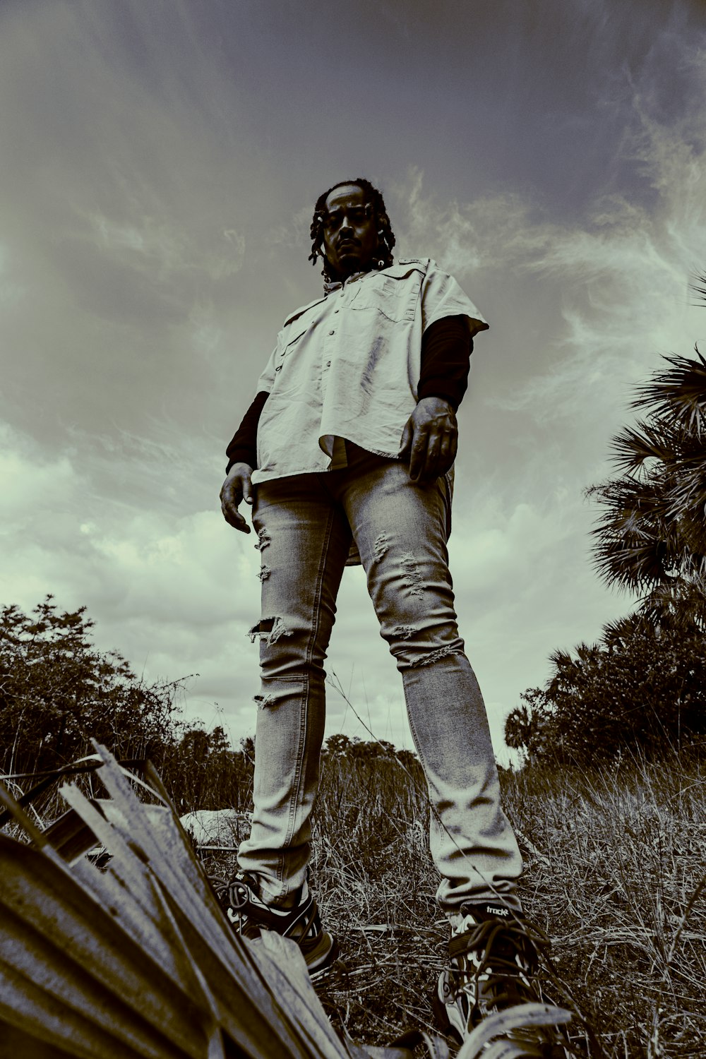 grayscale photo of man in white jacket and denim jeans standing on grass field