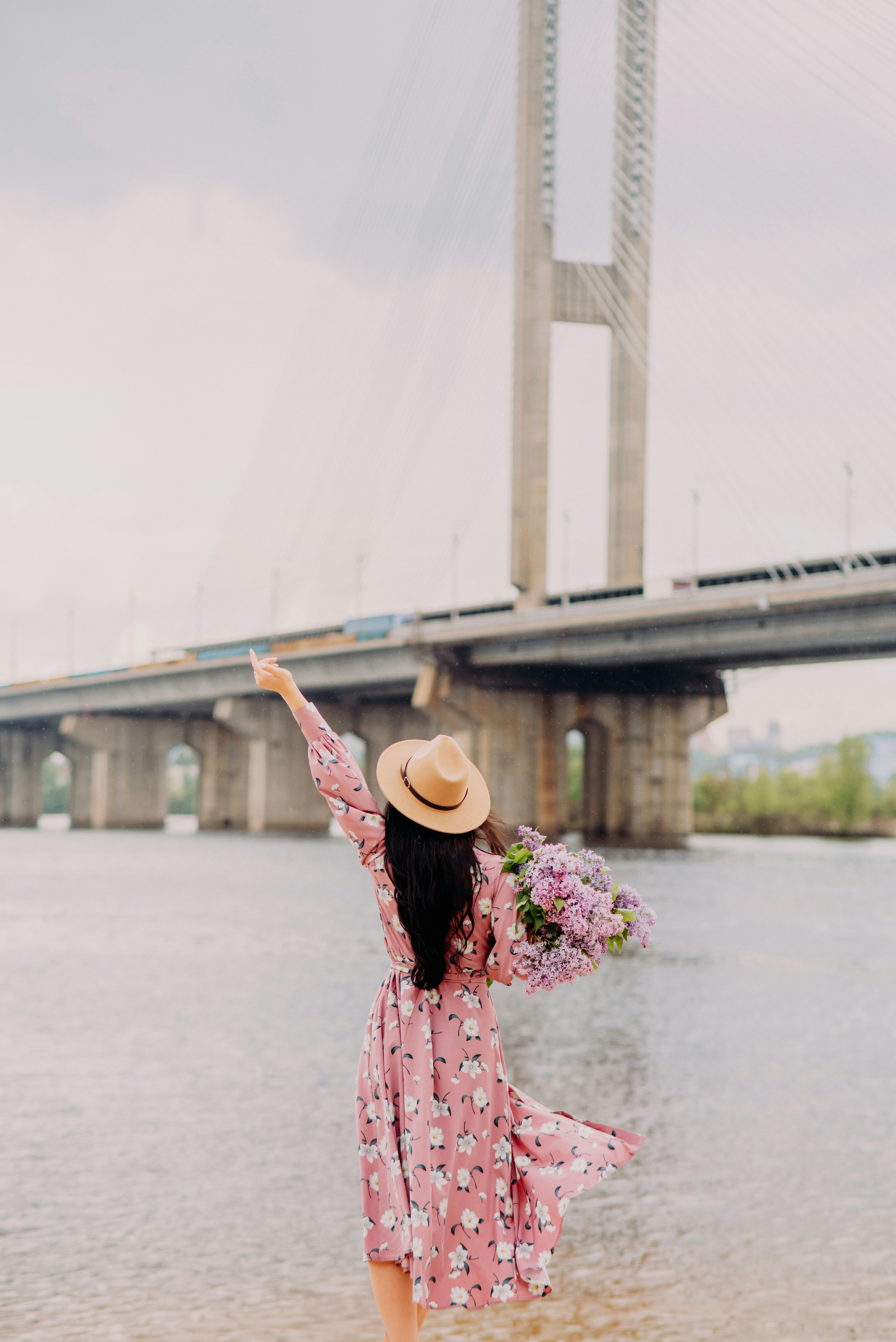 woman in pink floral dress wearing brown hat standing on gray concrete road during daytime