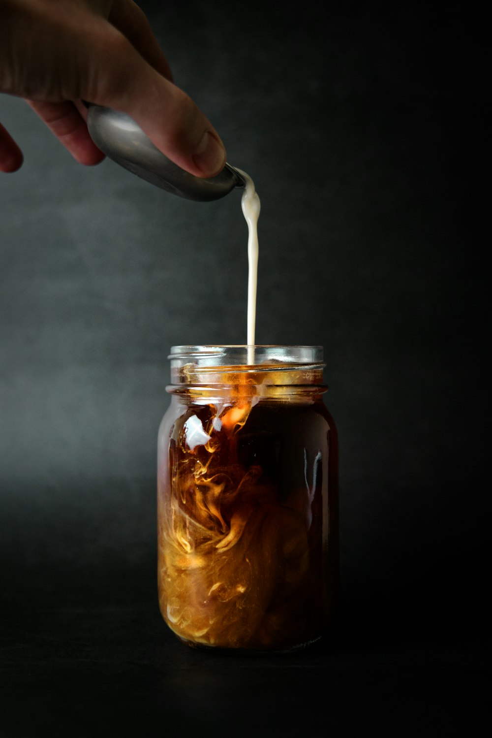 person holding clear glass jar with brown liquid