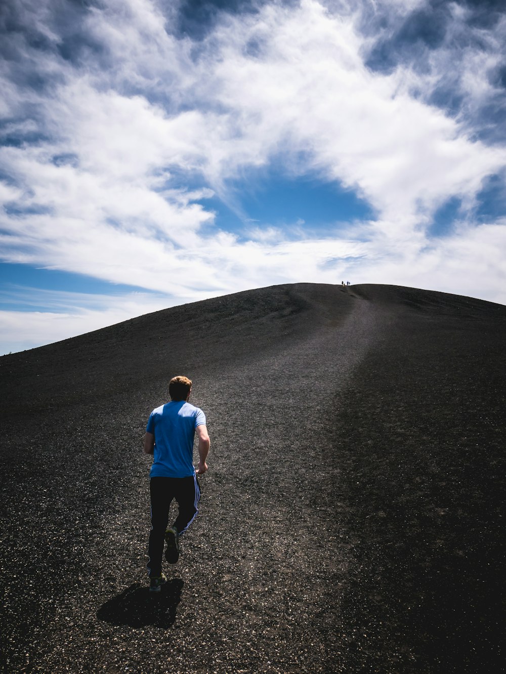 Homme en chemise blanche et jean en jean bleu debout sur le sable gris sous le ciel bleu pendant