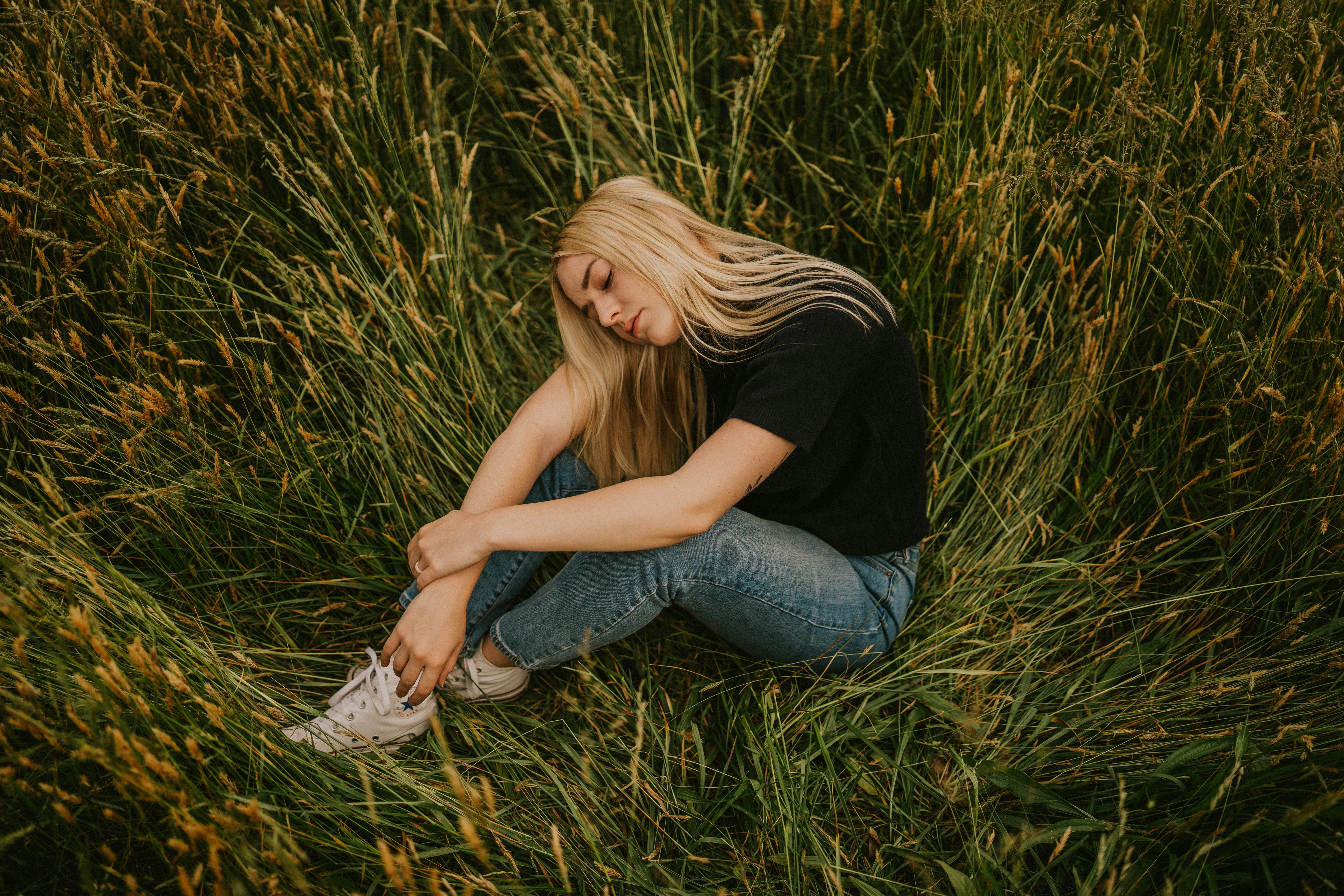 woman in black t-shirt and blue denim jeans sitting on grass field