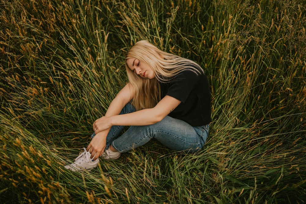 woman in black t-shirt and blue denim jeans sitting on grass field