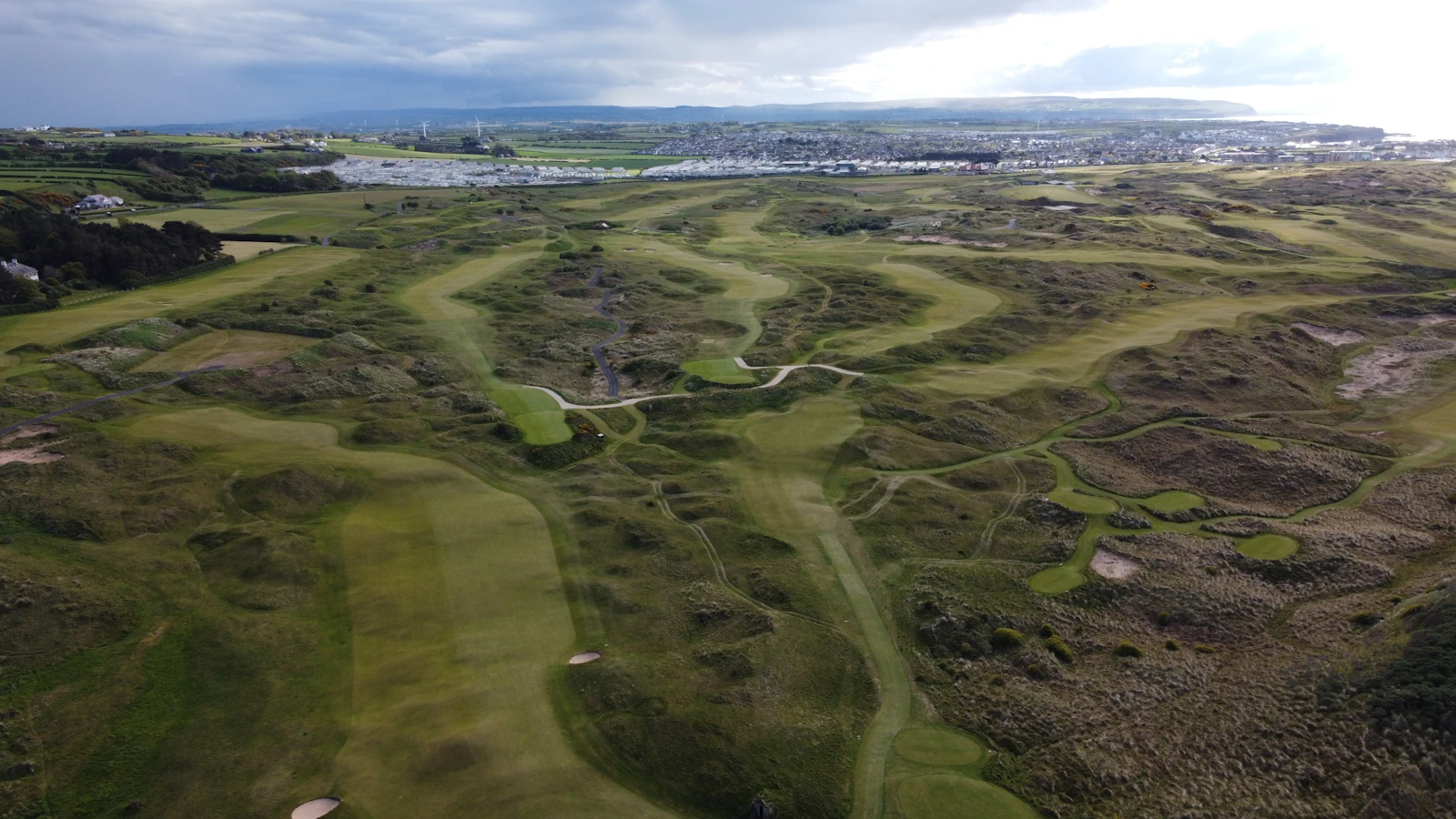 Aerial view of links fairways rolling toward the town