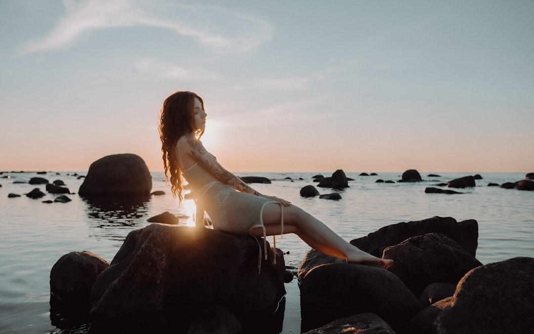 woman in white dress sitting on rock near body of water during daytime