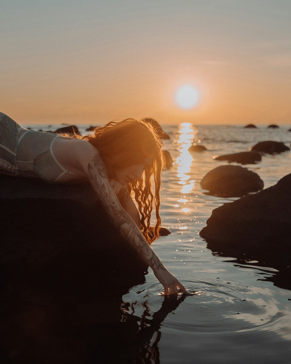 woman in white shirt and black pants standing on rock formation near body of water during