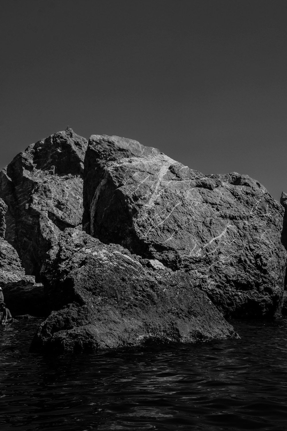 grayscale photo of rocky mountain near body of water
