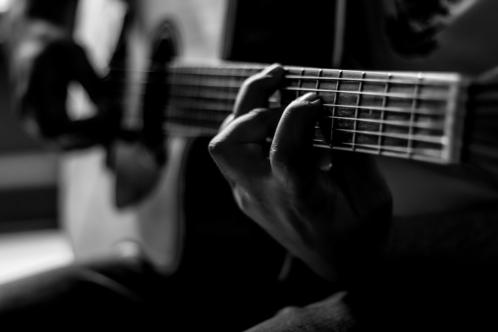 person playing guitar in grayscale photography