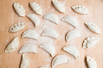A warm kitchen scene showing hands folding empanadas with fresh ingredients laid out nearby.