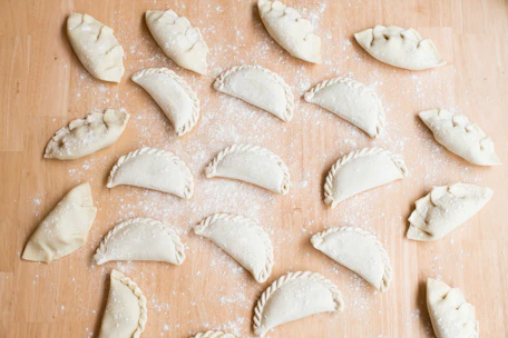 A warm kitchen scene showing hands folding empanada dough filled with savory ingredients.