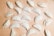 Multiple uncooked empanadas are arranged on a floured wooden surface. Each empanada is folded and sealed in a variety of styles, with some having intricate braided edges and others simple, rounded edges. The background is lightly dusted with flour, adding to the preparation theme.