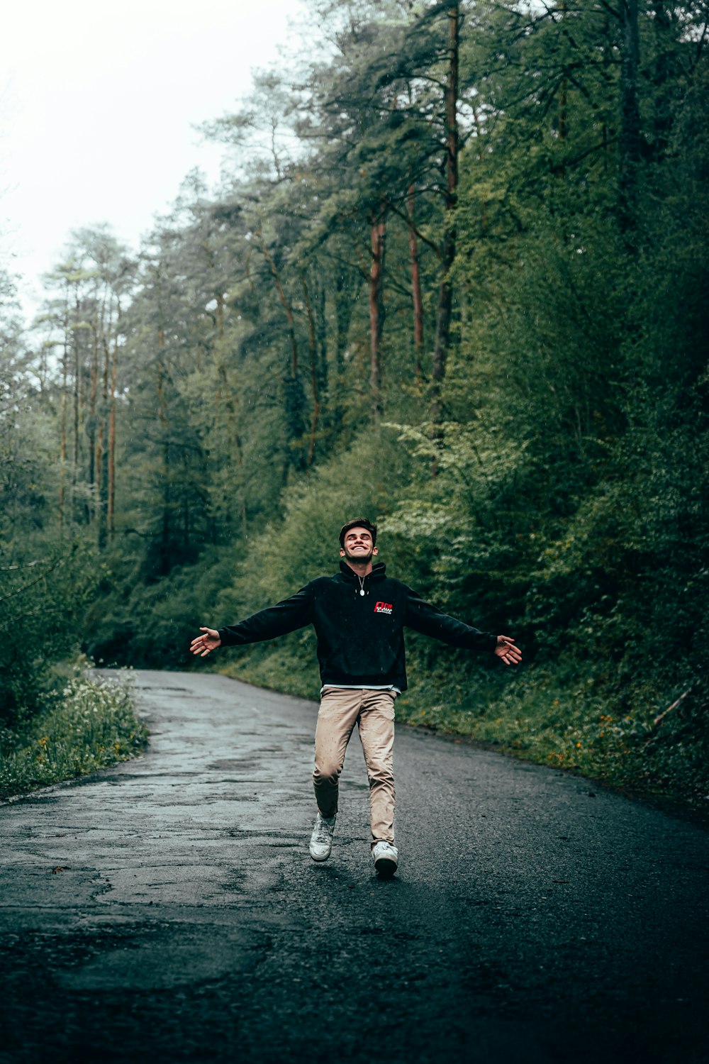 homme en chemise à manches longues noire et pantalon marron courant sur un chemin gris entre des arbres verts