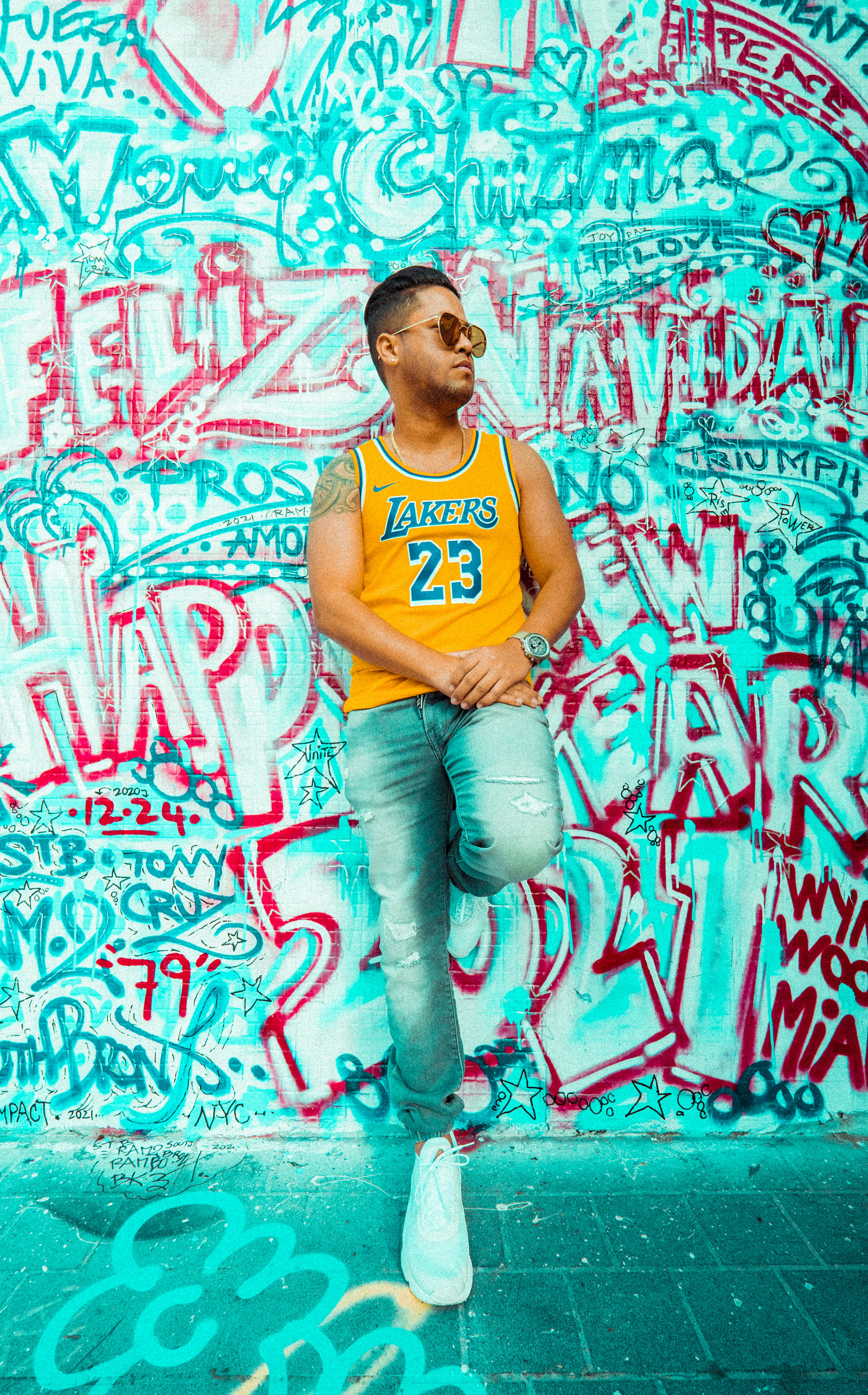 man in orange tank top and blue denim jeans standing beside wall with graffiti