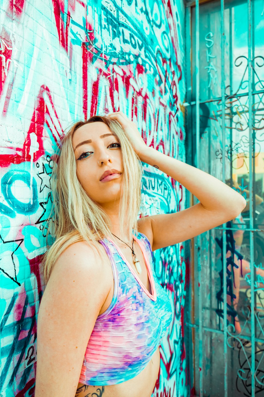 woman in pink and blue tank top leaning on wall with graffiti