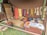 A rustic setup displaying a variety of yarns and woven textiles, with vibrant colors hanging from a tent. Basketfuls of colored yarns and wool are placed on the ground, and woven pieces are draped beside them. The ambiance suggests a traditional or artisanal craft setting.