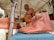 A craftsman demonstrates leatherwork under a tent. On display are brown leather shoes with decorative patterns, hung on a wooden structure. Additional leather goods are visible in the background. Attendees appear interested as they observe.