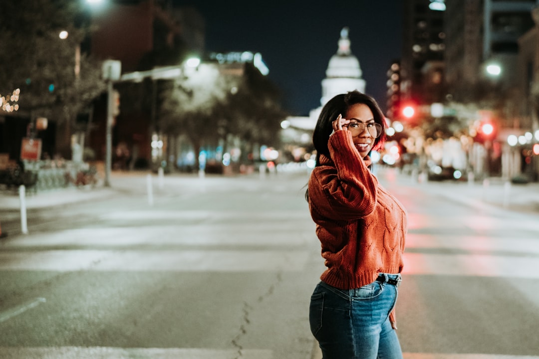 woman in brown jacket and blue denim jeans standing on road during daytime