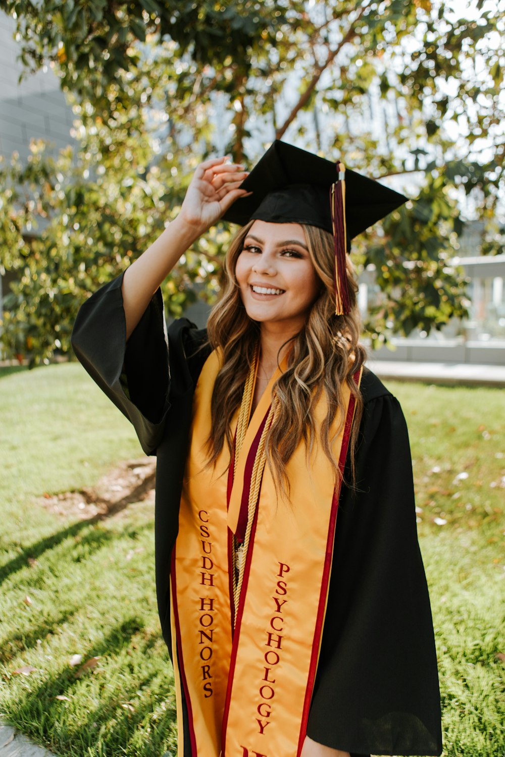 woman in black academic gown standing on green grass field during daytime