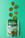 A packet of SuckerPunch Bread & Butter Pickle Chips is laid flat on a vibrant green surface. Several sliced pickle chips are arranged in an irregular pattern above the packet. The packaging prominently features a vintage-style illustration of a man in boxing attire, and includes labels emphasizing the product's snappy sweet flavor and non-GMO status.