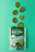 A packet of SuckerPunch Bread & Butter Pickle Chips is laid flat on a vibrant green surface. Several sliced pickle chips are arranged in an irregular pattern above the packet. The packaging prominently features a vintage-style illustration of a man in boxing attire, and includes labels emphasizing the product's snappy sweet flavor and non-GMO status.