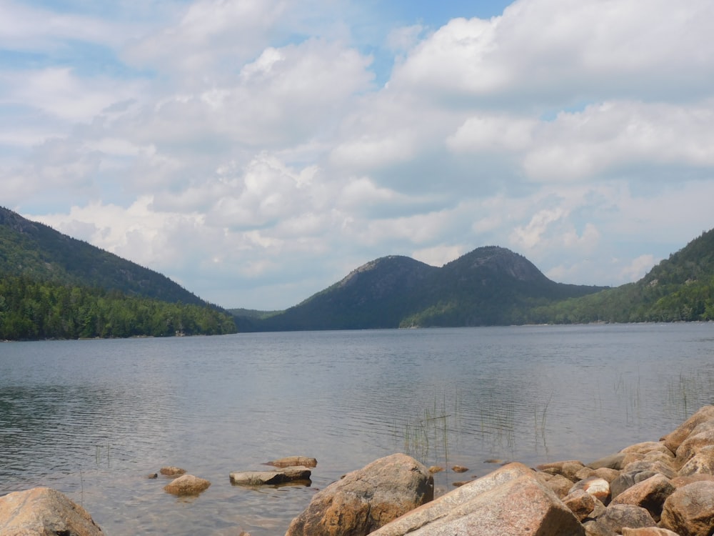 brown rocks on body of water near green mountains under white clouds during daytime