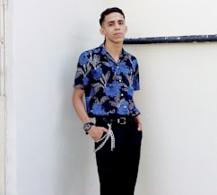 woman in blue and white floral button up shirt and black pants standing beside white wall