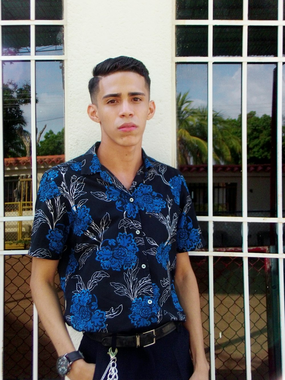 man in blue and white floral button up shirt standing near white metal fence during daytime