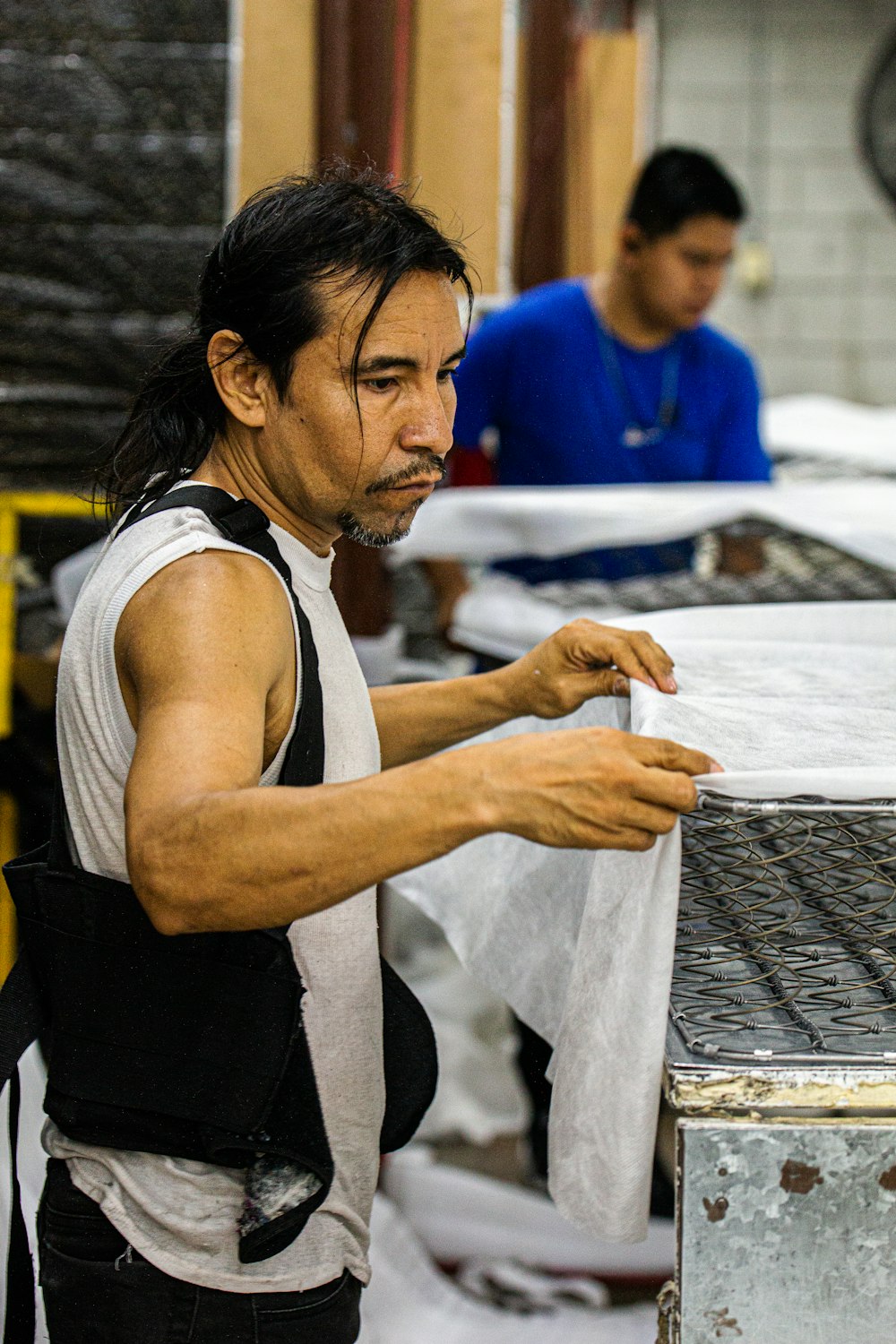 man in white tank top and black vest holding white printer paper