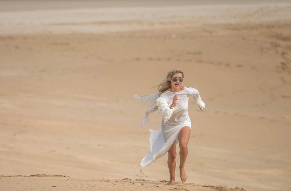 girl in white dress running on brown sand during daytime
