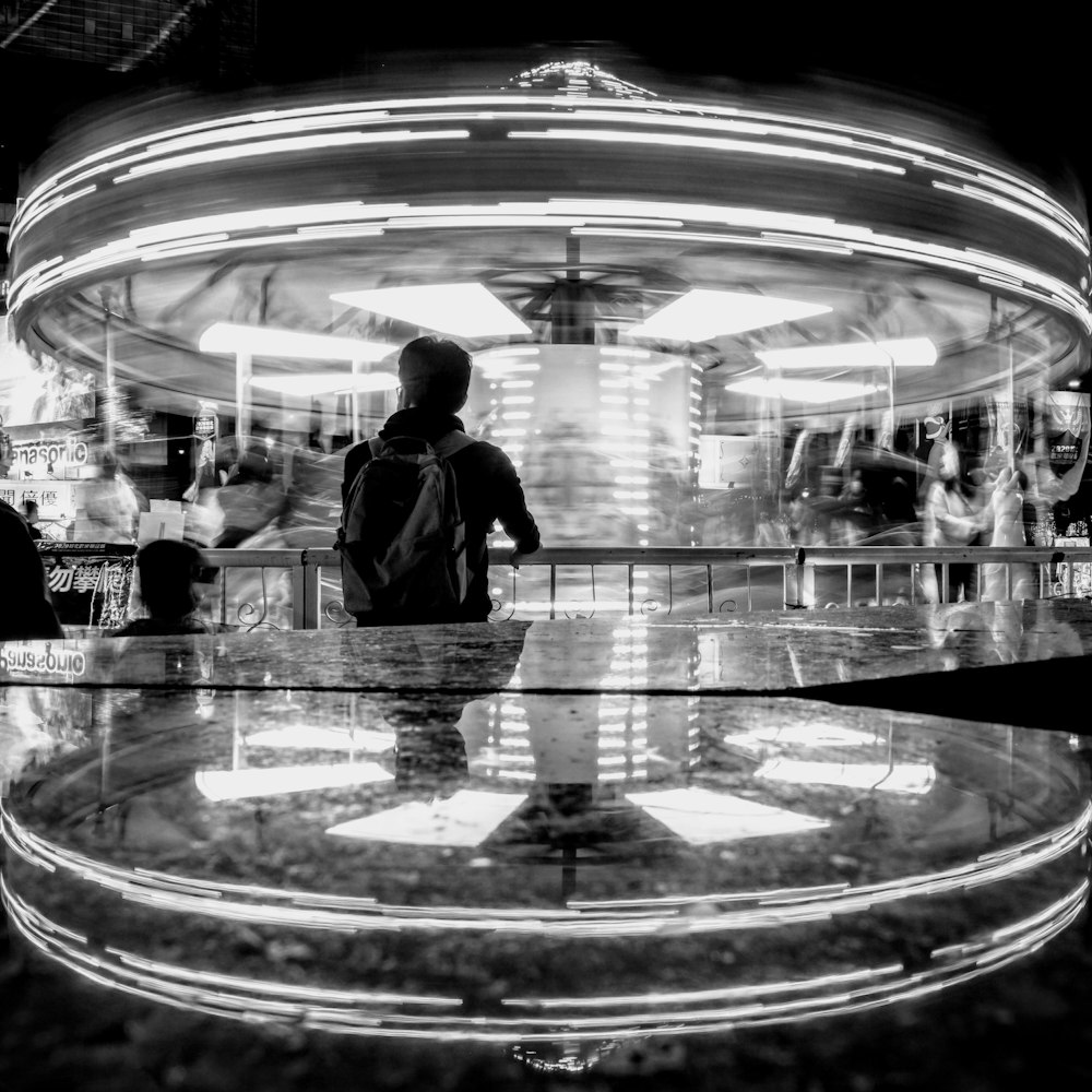 grayscale photo of man in black suit standing in front of glass wall