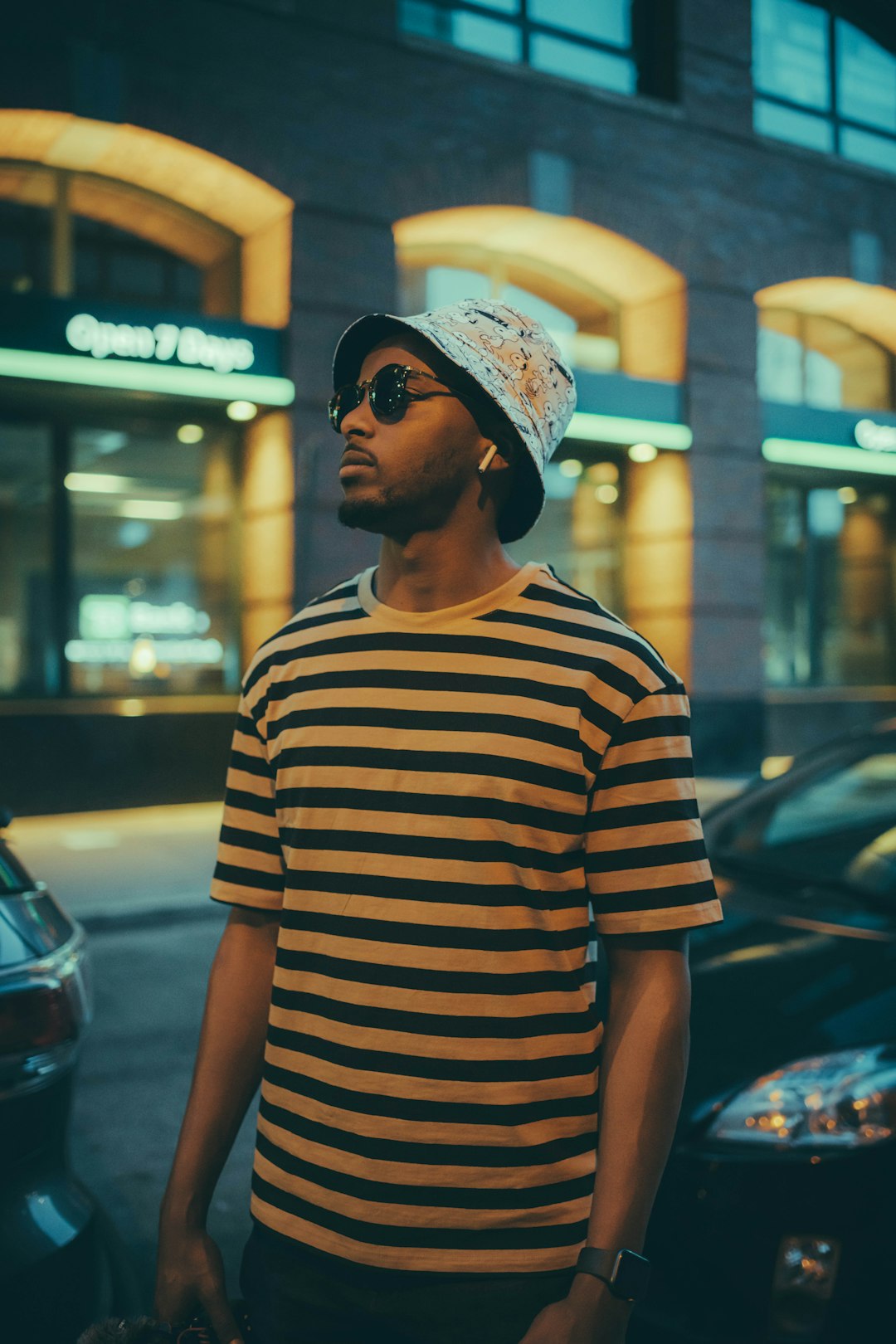 man in black and white striped crew neck t-shirt standing near glass wall during night