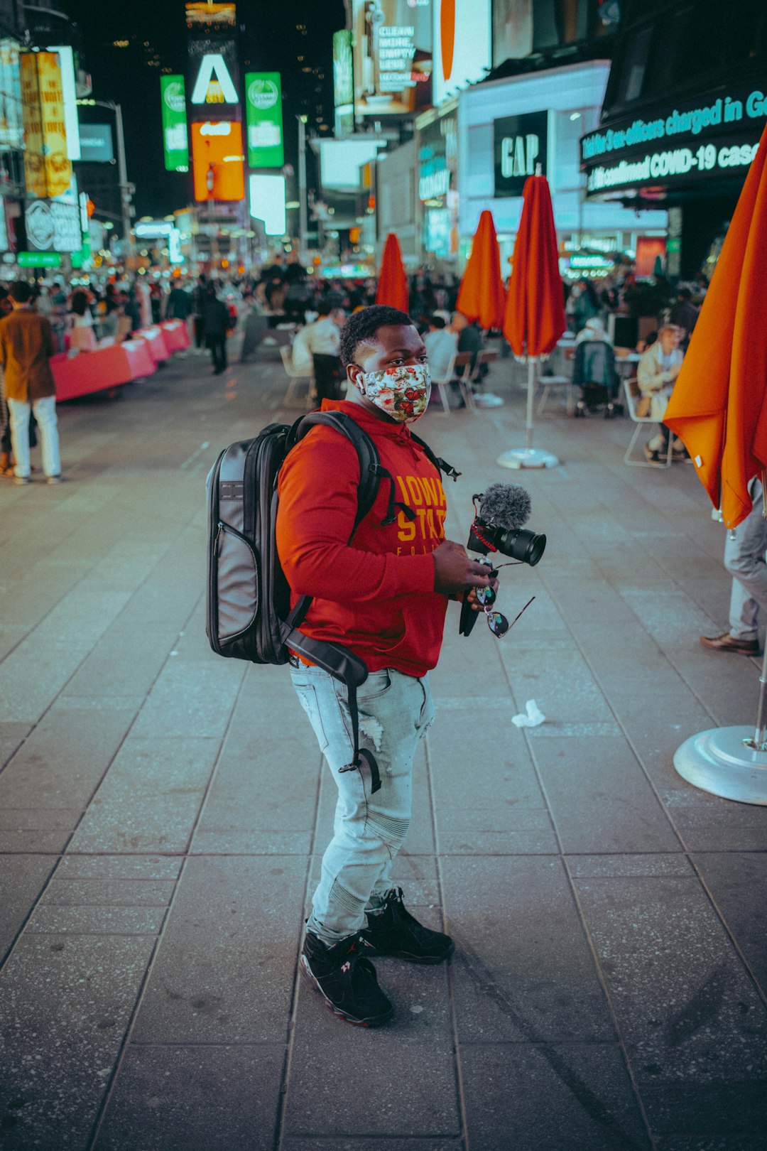 man in black and orange backpack and white pants walking on gray concrete floor