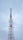 A tall communication tower with a red and white color scheme stands against a cloudy sky. Several antennas and satellite dishes are attached to the structure, indicating its use for broadcasting or telecommunications.