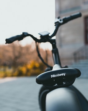 A close-up view of a Himiway bicycle seat with a blurred background. The bicycle is sleek and has a modern design. The focus is on the seat and part of the handlebars can be seen.