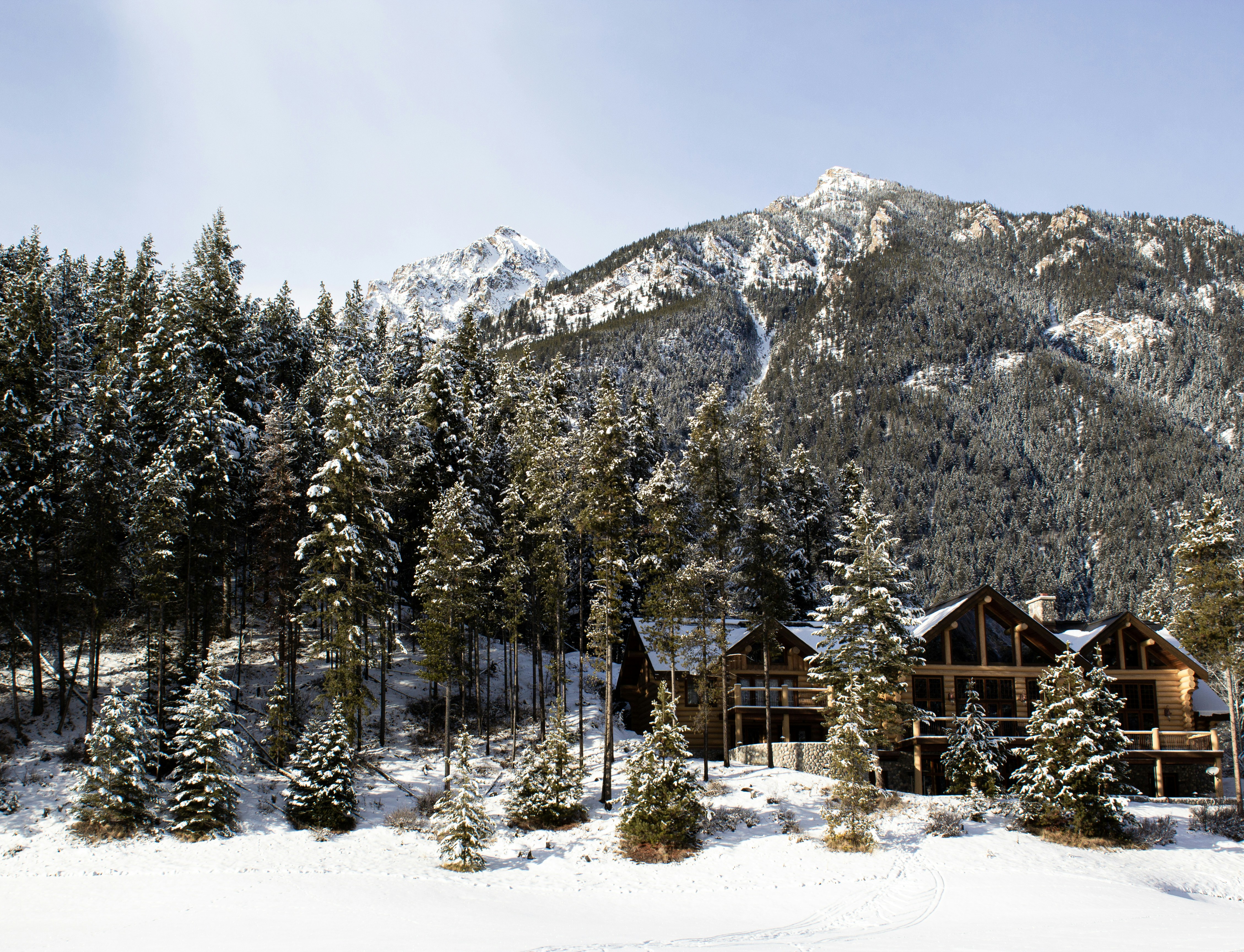 brown wooden house near green trees and snow covered mountain during daytime