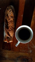 Rustic loaf of bread sliced open, steam rising, set on a wooden board beside a cup of coffee.