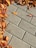 Concrete paving stones arranged in a grid pattern with a cluster of fallen autumn leaves along the edges, showcasing shades of orange, brown, and red.