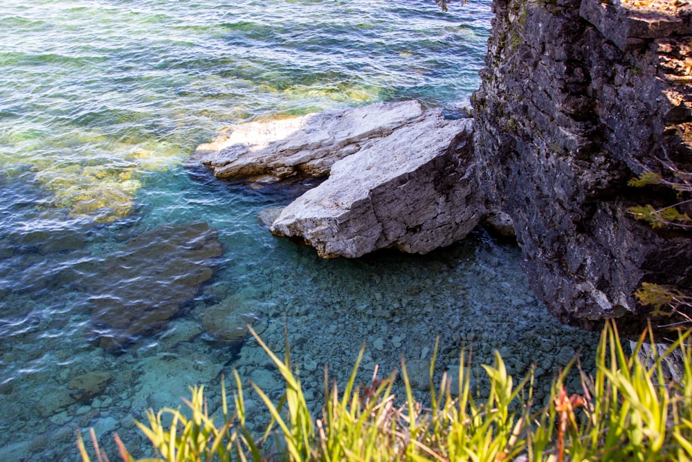 formação rochosa cinzenta ao lado do corpo de água durante o dia