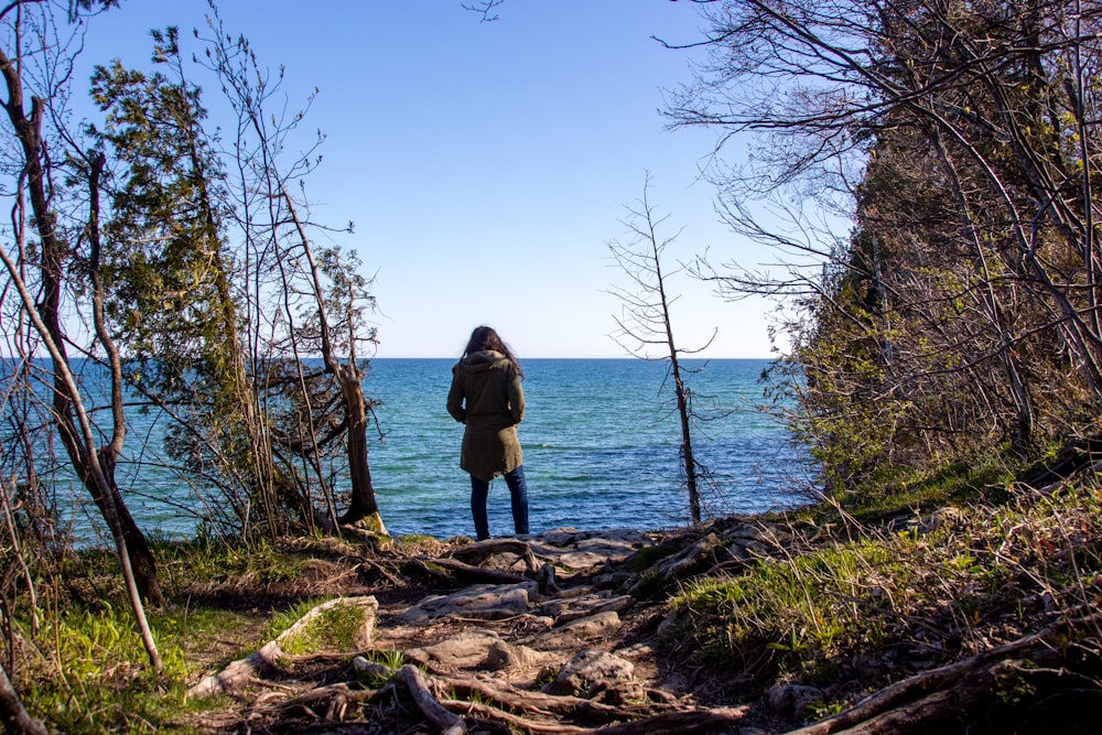 person in black jacket standing on brown log near body of water during daytime