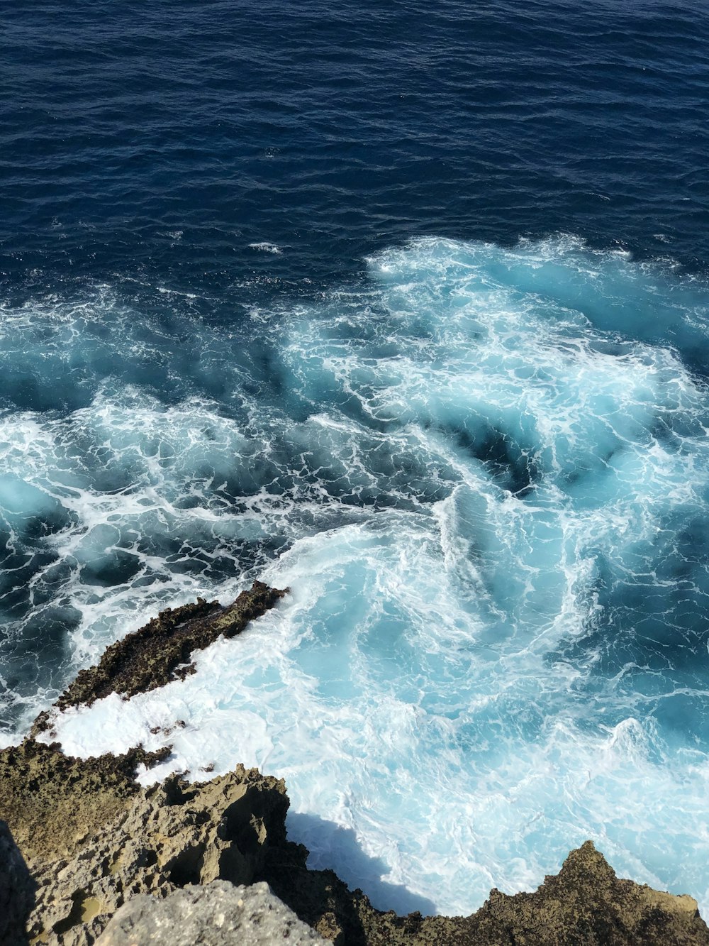 Olas azules del océano rompiendo contra la formación rocosa marrón durante el día