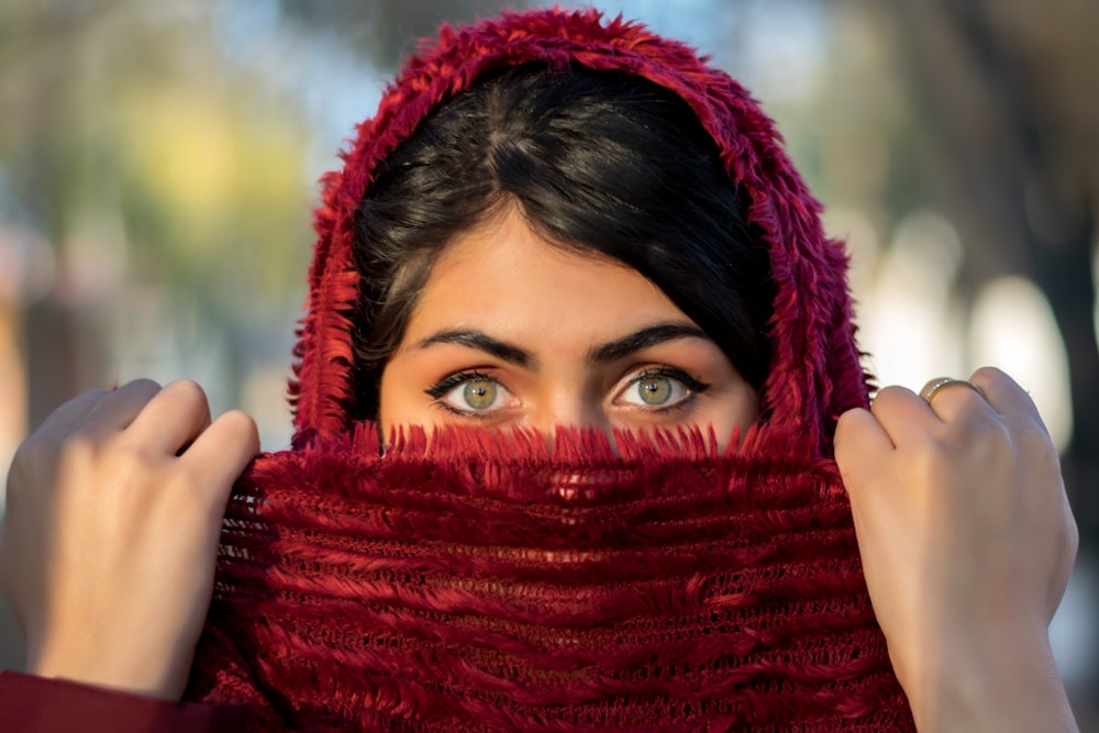 赤いヒジャブをかぶった女性が手で顔を覆っている