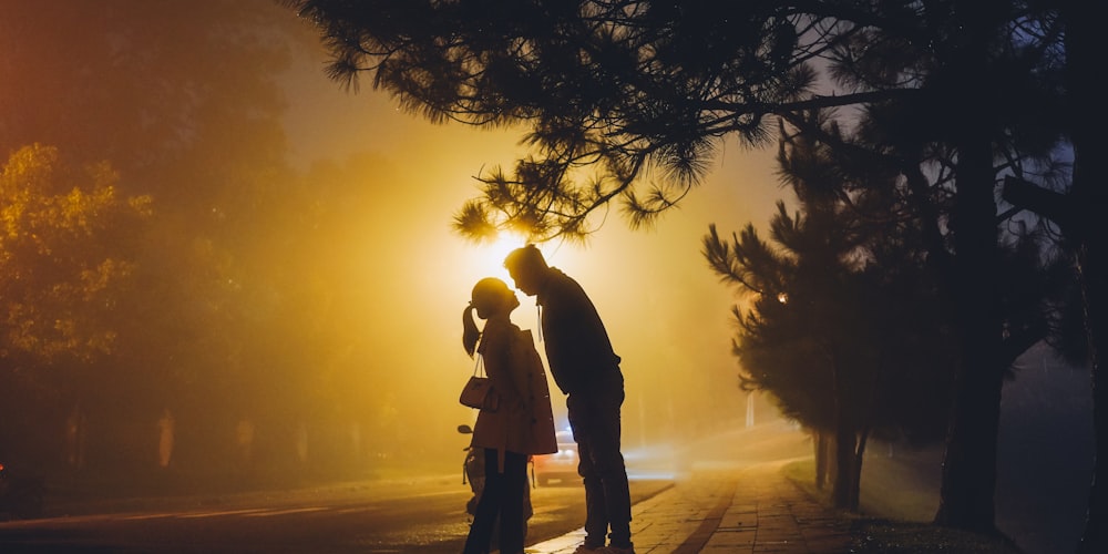 man and woman standing near tree during sunset