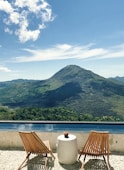 brown wooden table and chairs near lake and mountain under blue sky during daytime