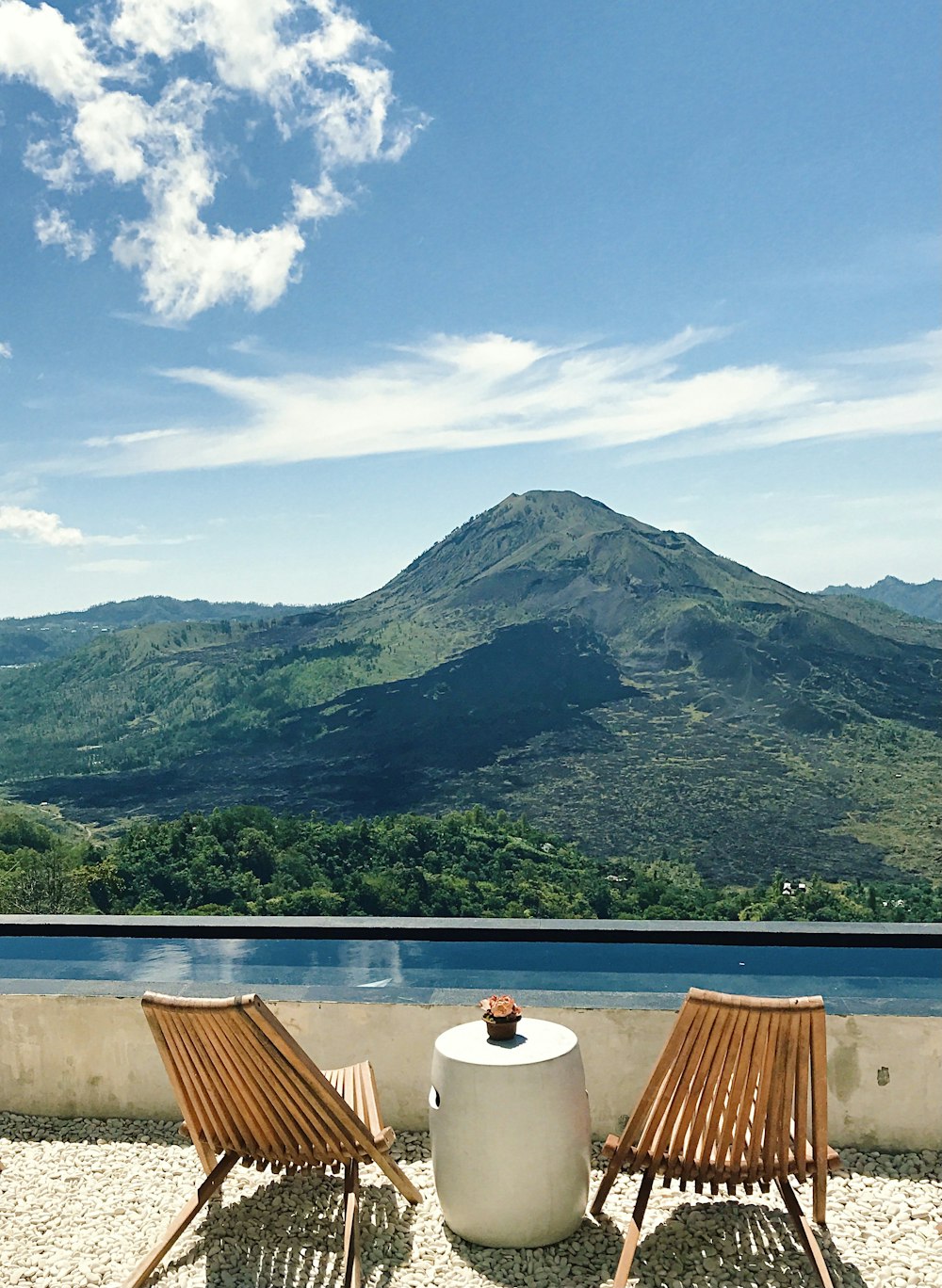 brown wooden table and chairs near lake and mountain under blue sky during daytime