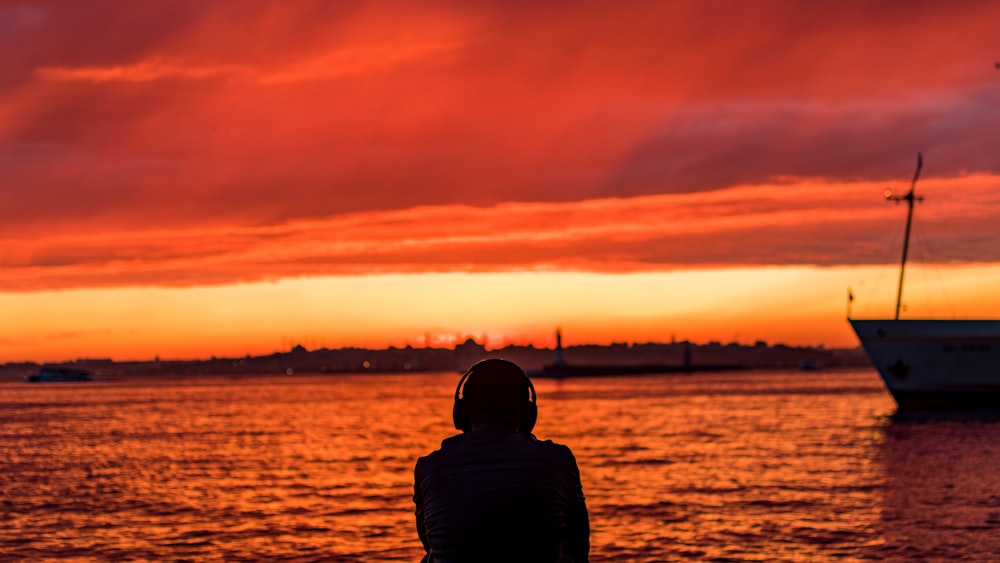 silhouette of man standing near body of water during sunset