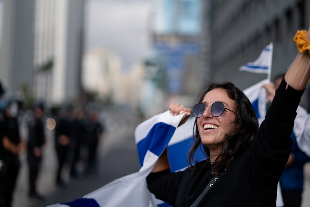 woman in black jacket wearing sunglasses holding white textile during daytime