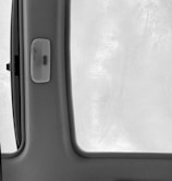A fogged and rain-specked car window is seen from inside, with condensation droplets dispersed across the glass. The window frame and a portion of the car interior, including a small panel or handle, are visible in the foreground.