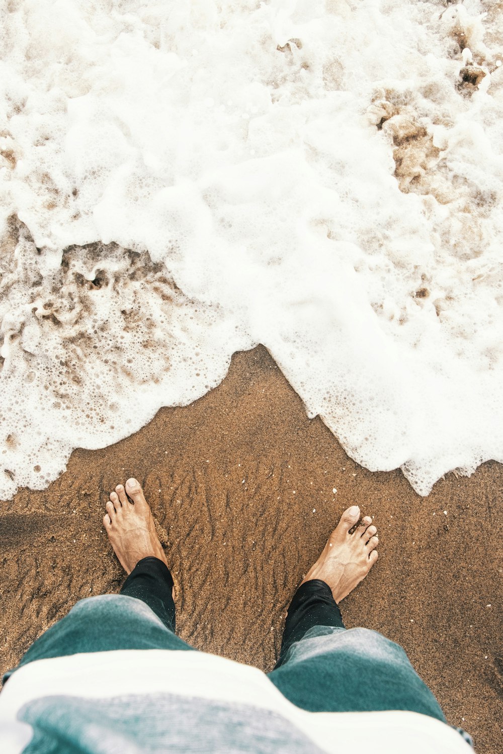 pessoa em pé na areia marrom perto do corpo de água durante o dia